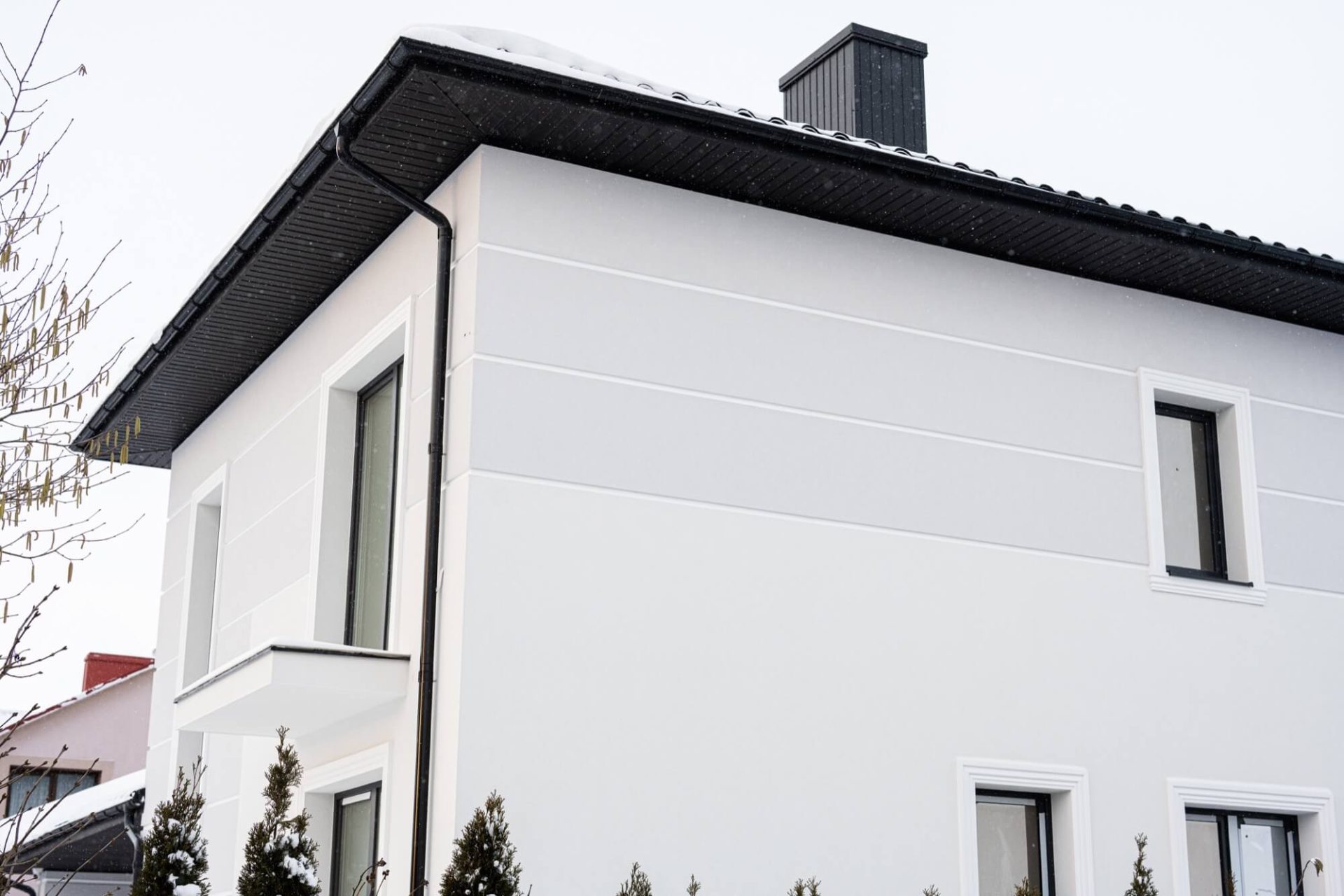 En vit husfasad som nyligen renoverats, med svarta detaljer på taket, fotograferad under en snörik vinter